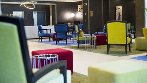 Een hotel lobby met diverse zithoeken, waaronder blauwe en gele stoelen, rode en gele poefs en een moderne kroonluchter.