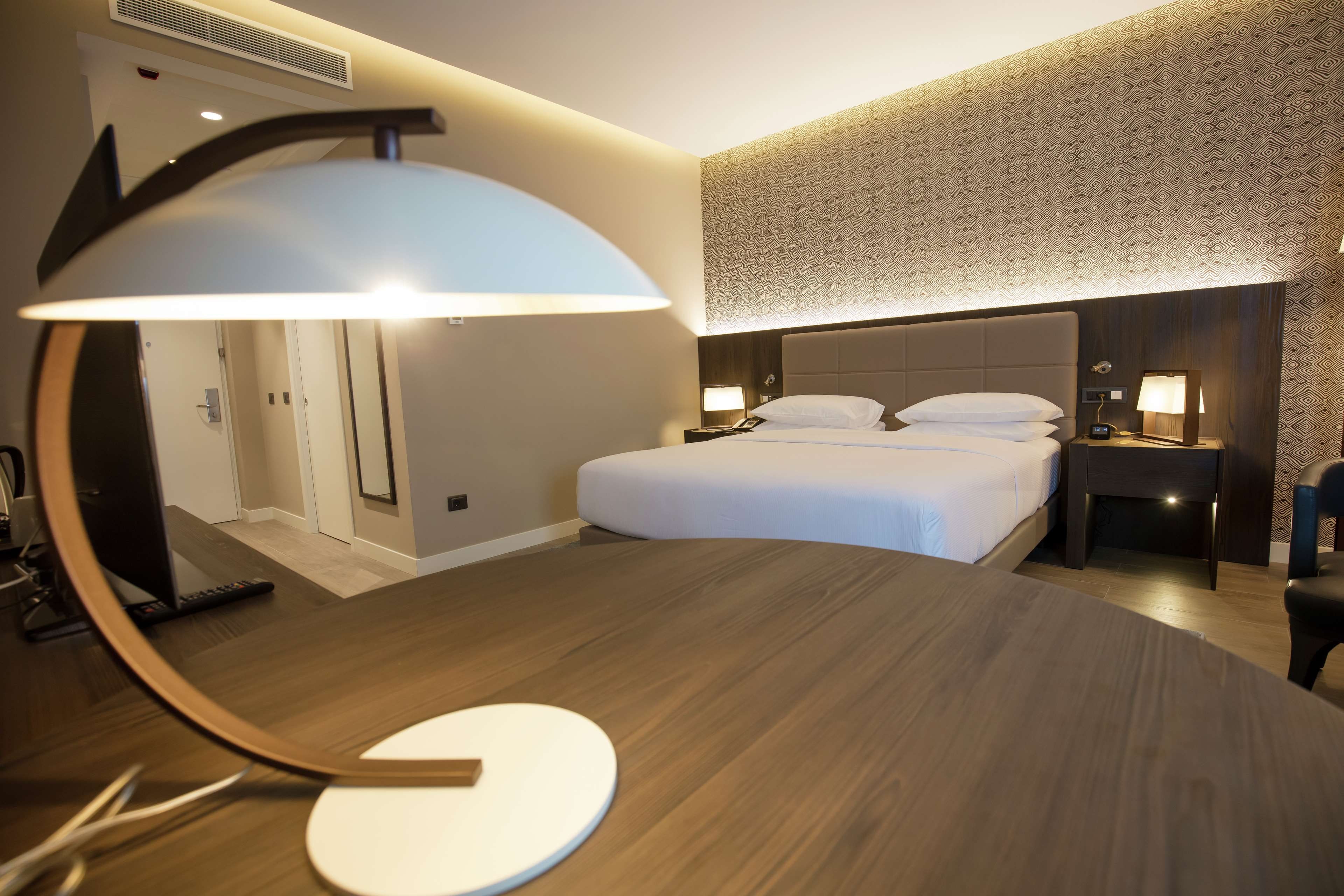 Une chambre d’hôtel avec un lit, des tables de chevet, un bureau et un miroir.