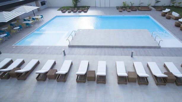 A swimming pool with sun loungers and tables, surrounded by a tiled deck. - Doubletree by Hilton Pointe-Noire (Pointe-Noire)