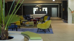 Eine moderne Lobby mit verschiedenen Sitzgelegenheiten, darunter gelbe und blaue Stühle, ein runder Couchtisch und ein Blumentopf.