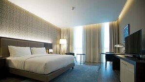 Ein modernes Hotelzimmer mit einem großen Bett, einem Schreibtisch, einem Fernseher und Blick auf die Stadt.
