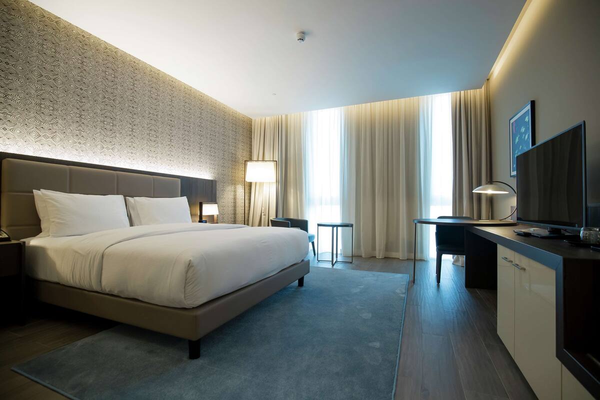 Ein modernes Hotelzimmer mit einem großen Bett, einem Schreibtisch, einem Fernseher und Blick auf die Stadt.