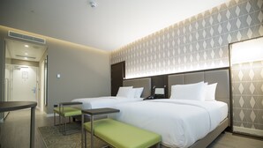 A hotel room with two beds, a bench, a small table, and a patterned wall. - Doubletree by Hilton Pointe-Noire (Pointe-Noire)