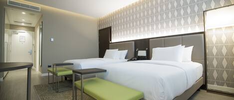 A hotel room with two beds, a bench, a small table, and a patterned wall.