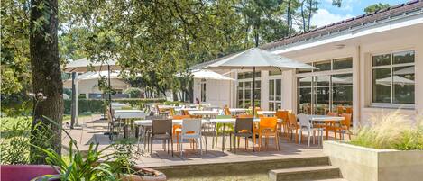 An outdoor patio area with tables and chairs, surrounded by trees and potted plants.