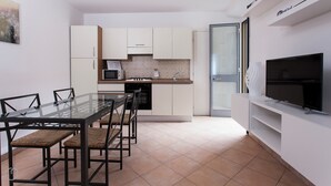 A compact kitchen with white cabinets, a microwave, a stove, and a built-in oven. There is a dining table with chairs and a flat-screen TV mounted on the wall. - Italianway - Vigevano 45 (Milan)