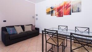 A modern living room with a black sofa, colorful cushions, a glass dining table with chairs, and abstract wall art. - Italianway - Vigevano 45 (Milan)