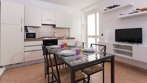 A modern kitchen with white cabinetry, a dining table set for four, and a flat-screen TV mounted on the wall. - Italianway - Vigevano 45 (Milan)