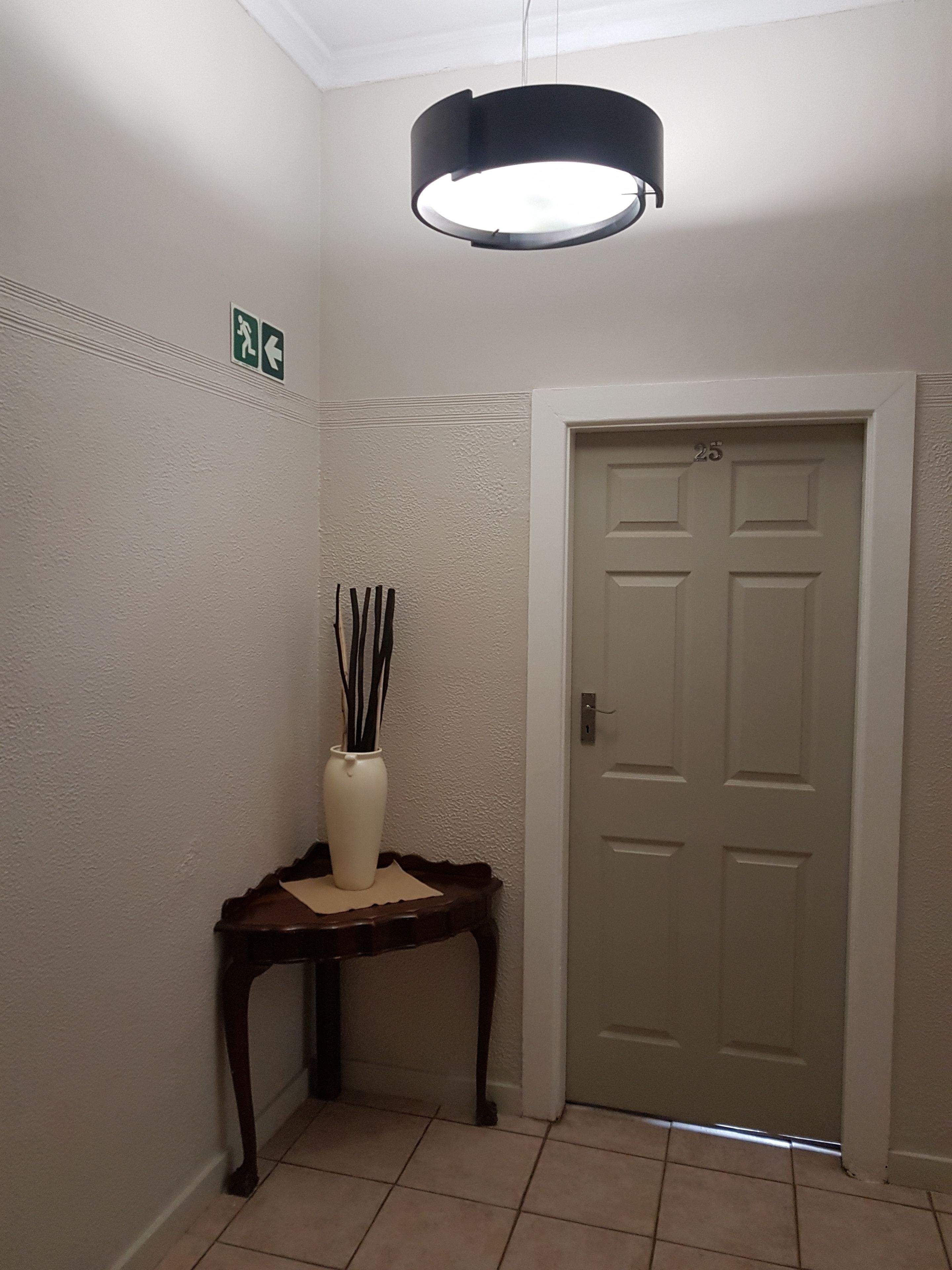 A hallway with a white door marked with the number 25, a small table with a vase, and a ceiling light fixture.