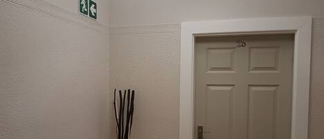 A hallway with a white door marked with the number 25, a small table with a vase, and a ceiling light fixture.