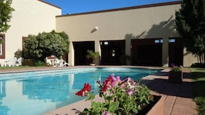 Una piscina con superficie de agua azul cristalina, rodeada por un sendero de ladrillo y una jardinera con flores.