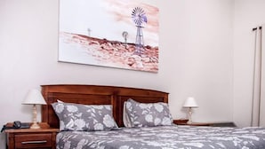 Un dormitorio con cabecera de madera, dos mesitas de noche con lámparas, una cama con colcha de estampado floral y un cuadro colgado en la pared que representa un molino.