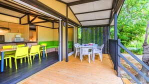 A covered outdoor dining area with a wooden deck, yellow chairs, and a table. - Village Vacances Azureva Sigean (Sigean)