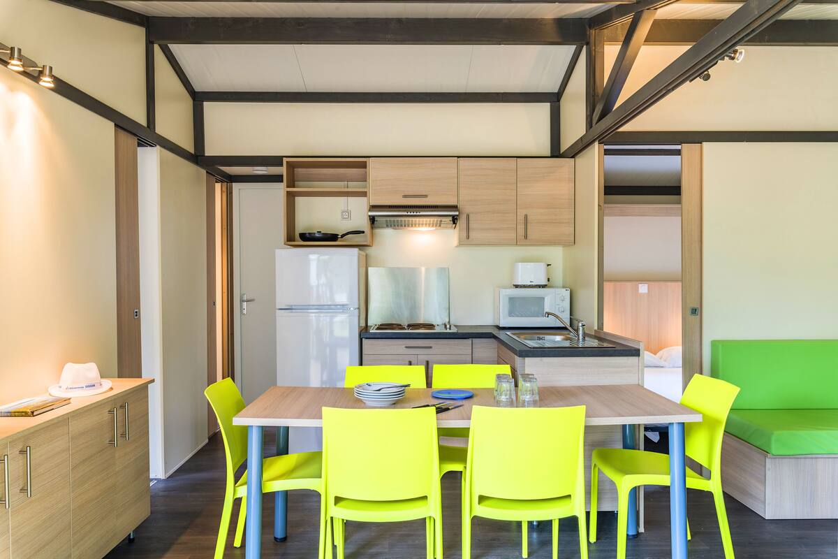 A compact kitchen with modern appliances, a dining area with bright yellow chairs, and a green sofa in a small living space.