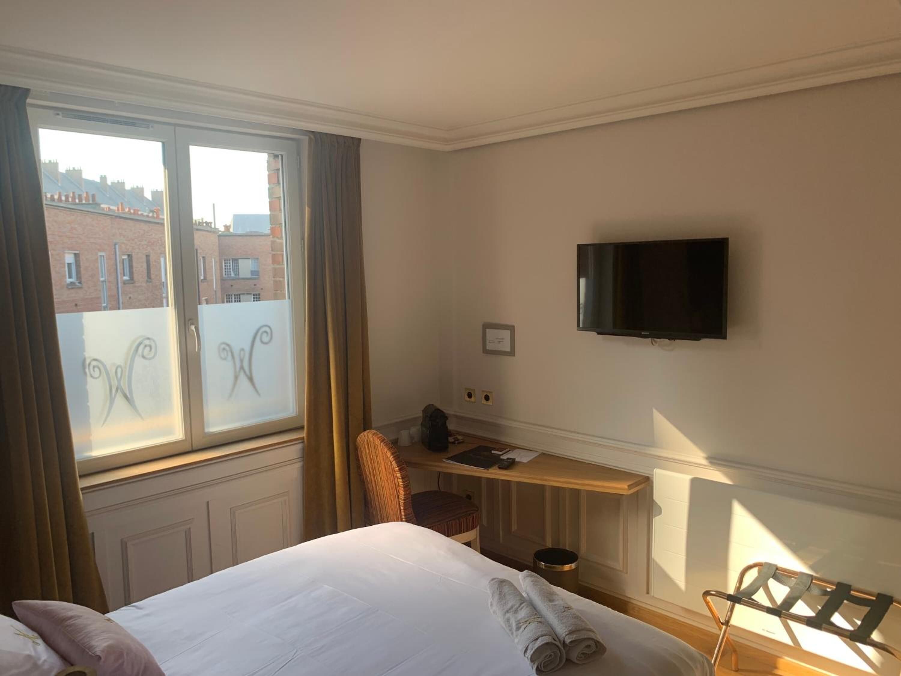 Une chambre d’hôtel équipée d’un lit, d’un bureau, d’une chaise, d’une télévision et d’une fenêtre avec des rideaux.