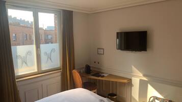 Une chambre d’hôtel équipée d’un lit, d’un bureau, d’une chaise, d’une télévision et d’une fenêtre avec des rideaux.