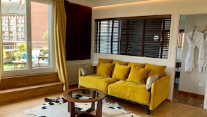 Una habitación con un sofá amarillo, una mesa de centro redonda de madera y una alfombra de cuero de vaca.