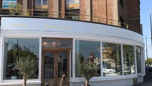 Un hotel con restaurante en la planta baja, con amplias ventanas y plantas en macetas.