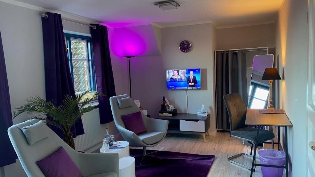 A modern living room with a flat-screen TV, a desk, and two chairs.