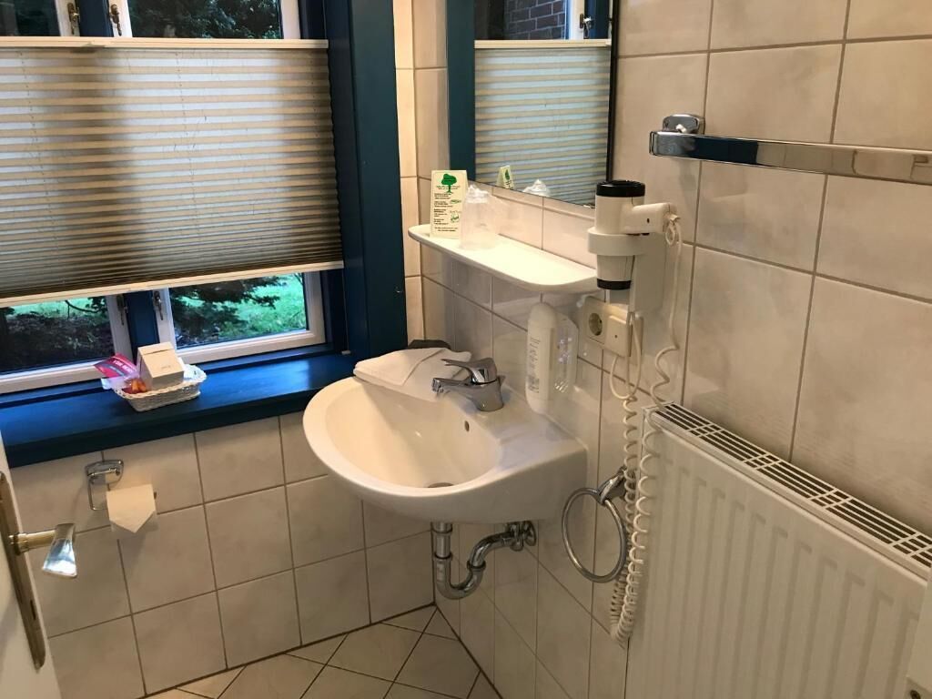 Baño con lavamanos, espejo, ventana con persianas y radiador.