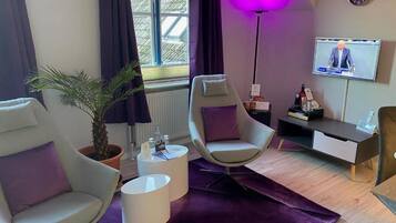 Un salon moderne avec un canapé, un fauteuil et un téléviseur diffusant un journal télévisé.