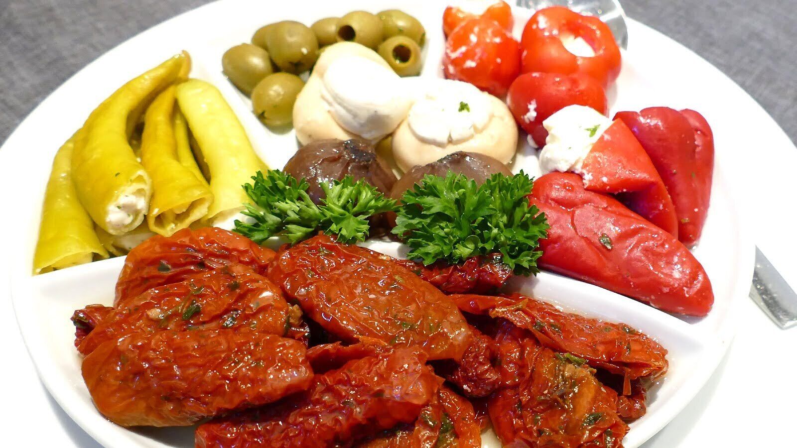 A plate of food with various items including tomatoes, olives, and a green garnish.