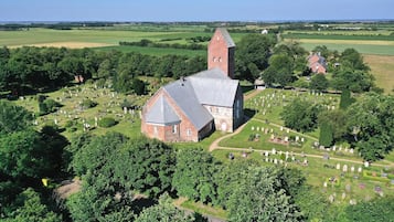 An aerial view of a church with a prominent tower, surrounded by a cemetery with neatly arranged gravestones and lush greenery.