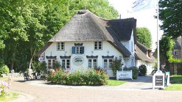 En traditionel bygning med stråtækt tag, nummererede vinduer og et skilt, der angiver, at det er en restaurant.