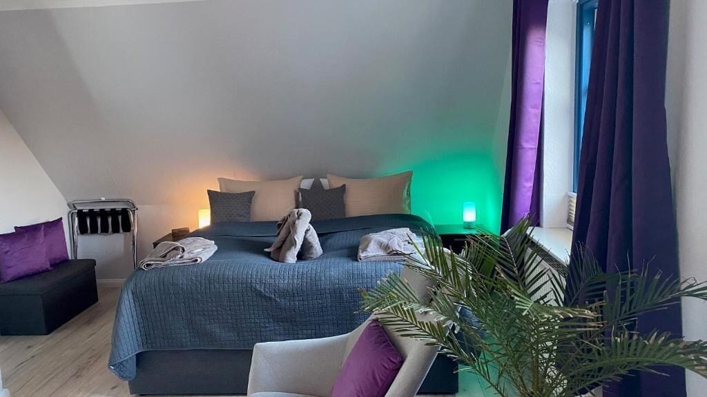 Ein modernes Schlafzimmer mit einem Bett, einem Sessel, einem Nachttisch und einer Pflanze.