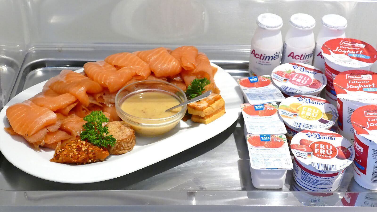 Ein Kühlschrank mit Lachs, Joghurt und einer kleinen Schale Soße.