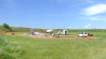 En campingplads med telte, en campingvogn og en hvid varevogn.