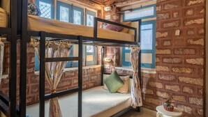 Habitación con literas, pared de ladrillo, una pequeña mesa con una planta y una ventana con cortinas.