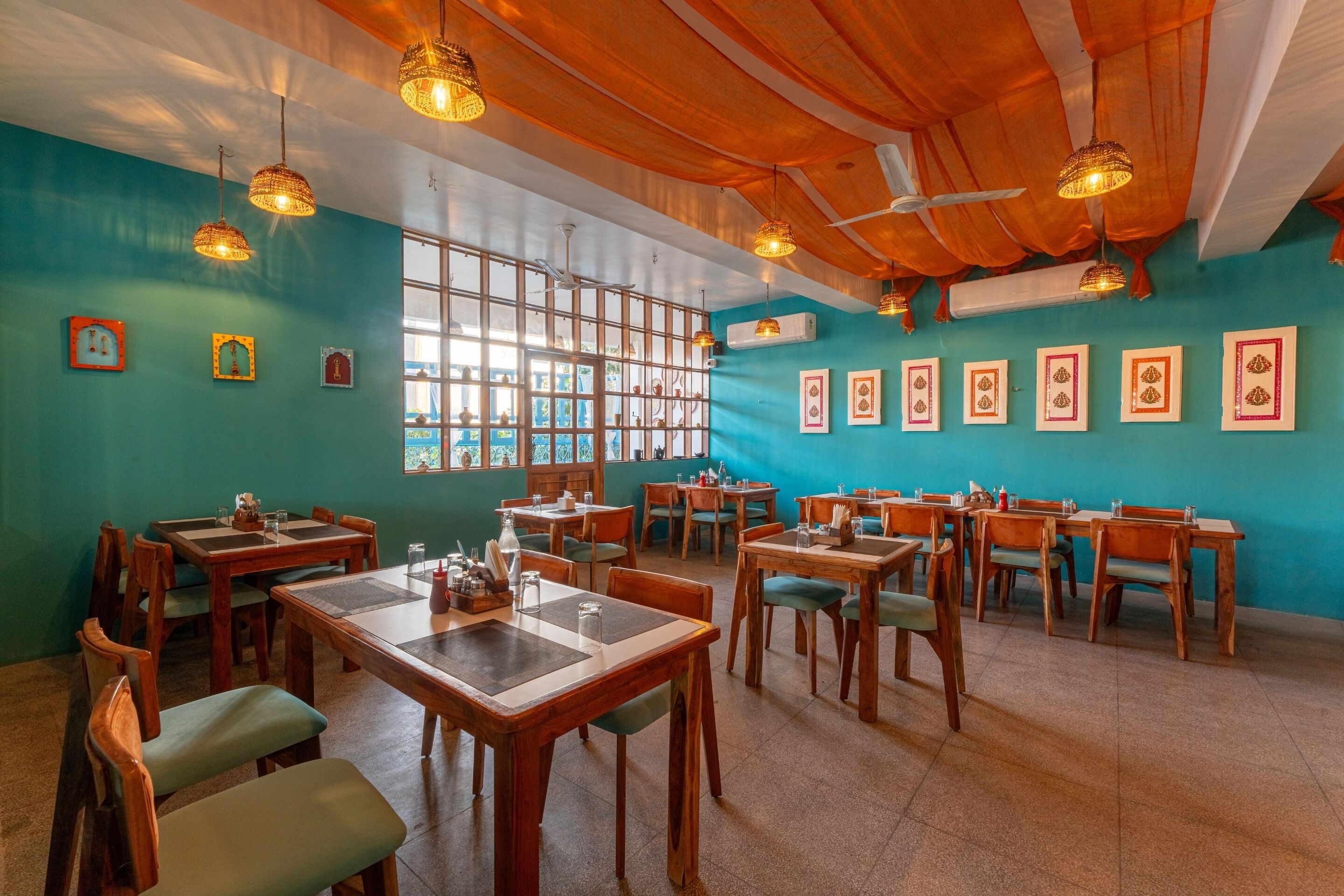 A restaurant with wooden tables and chairs, teal walls, and hanging light fixtures.