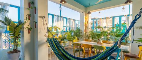 A spacious patio with a hammock, dining table, chairs, and potted plants.