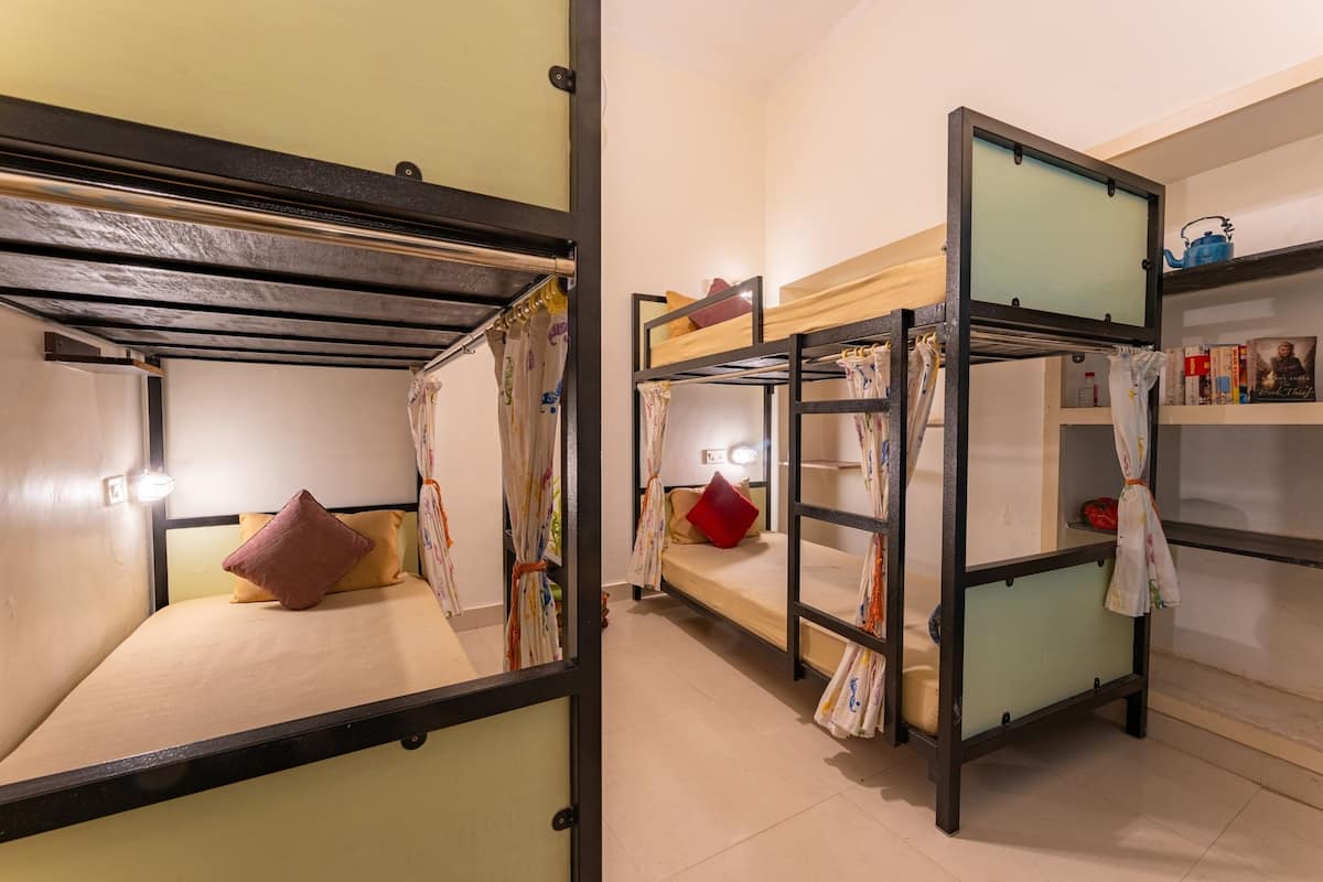 Une chambre de dortoir avec des lits superposés, une petite étagère avec des livres et un rideau.