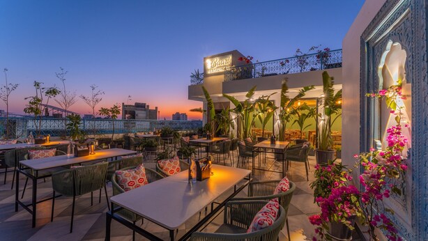 Un área de comedor al aire libre con mesas y sillas, un letrero que dice 'Baari Restaurant' y plantas en macetas.