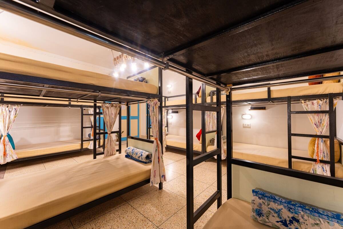 Une chambre de type dortoir, avec des lits superposés, un petit bureau et une fenêtre avec des rideaux.