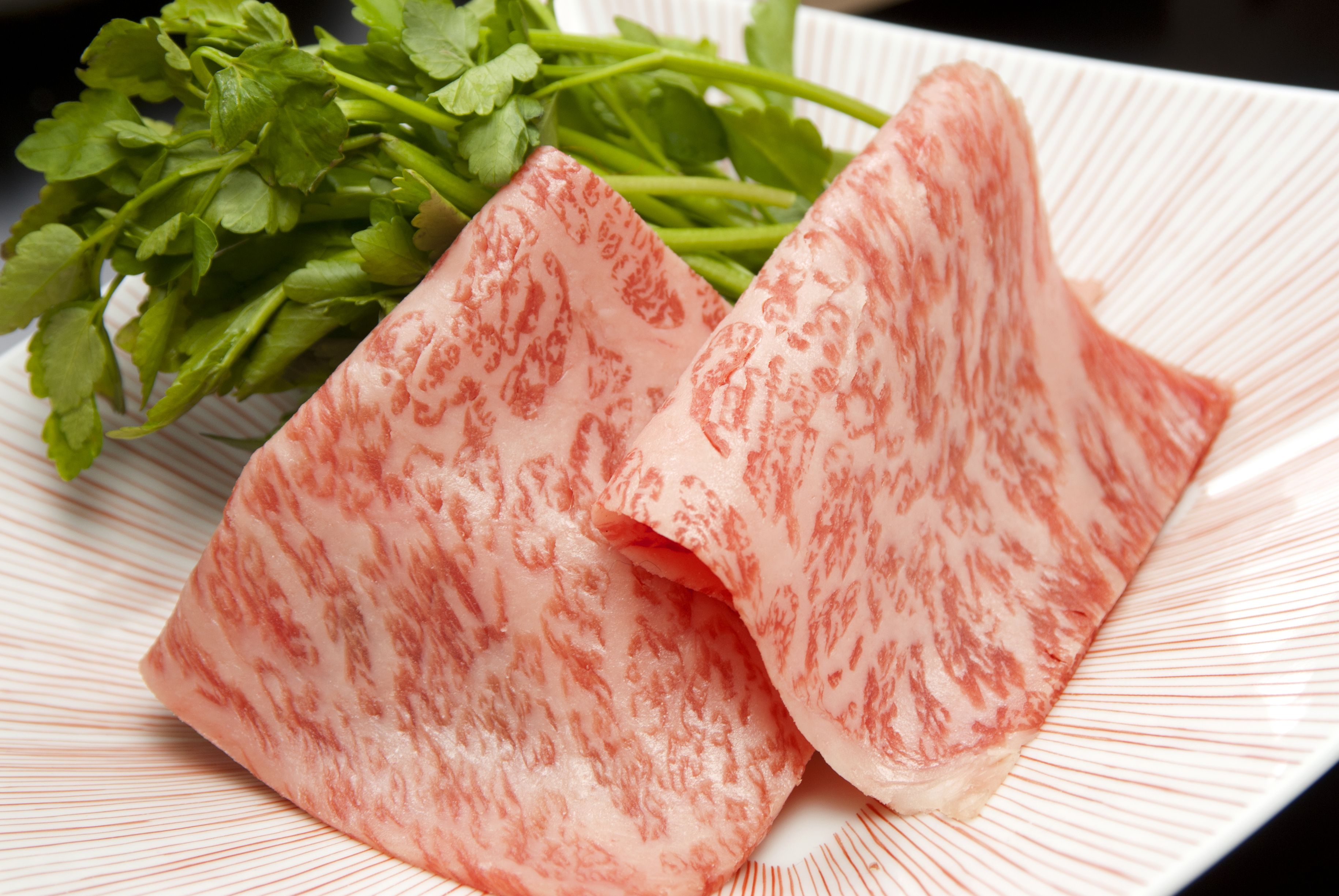 A plate with sliced meat and green herbs.