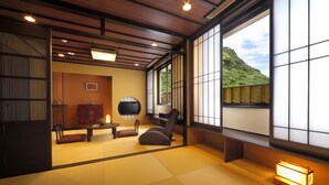 Une pièce de style japonais traditionnel, avec un sol recouvert de tatamis, une table basse, un canapé et un téléviseur.