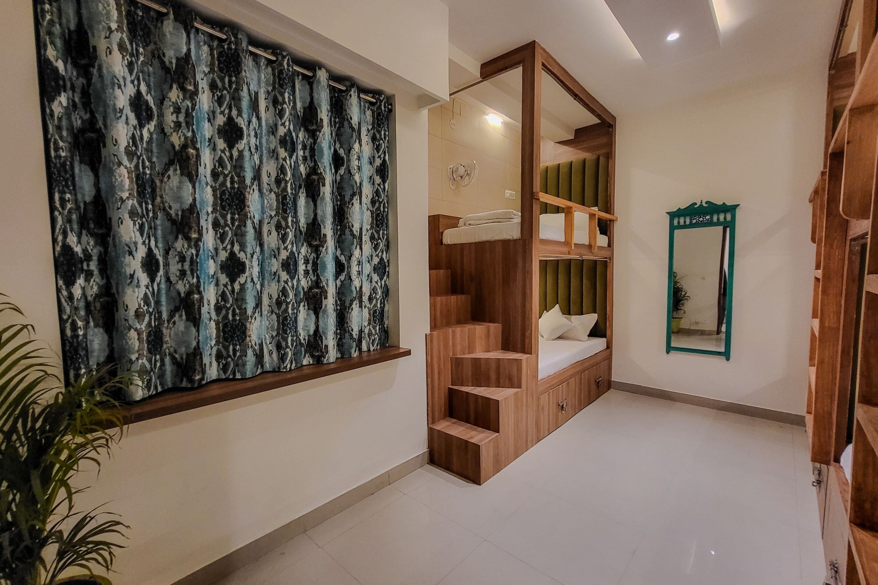 Habitación de hotel con un ventanal grande, una escalera de madera integrada, un banco acolchado verde y un espejo en la pared.