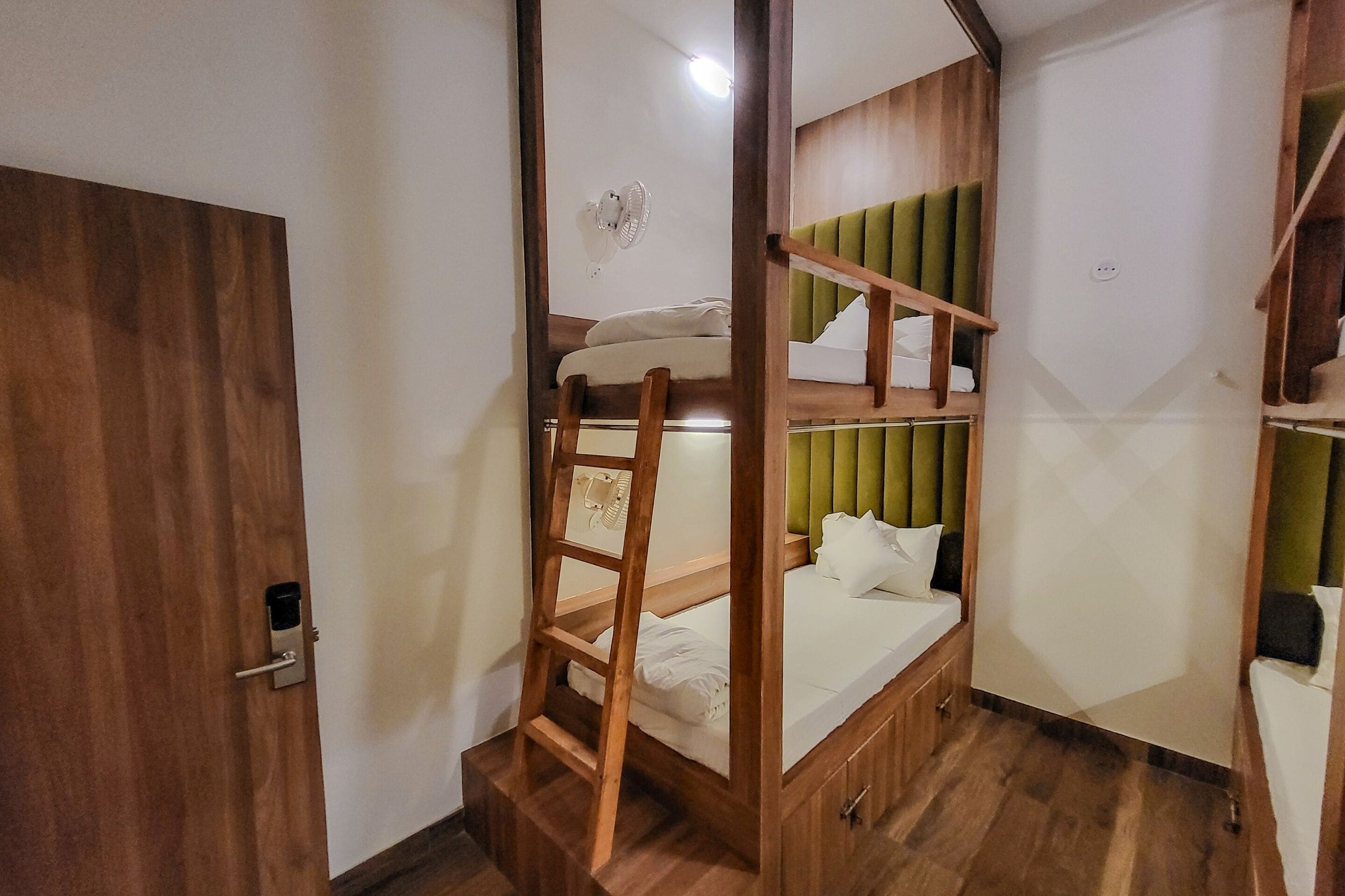 Een kamer met stapelbedden, een houten ladder en een kleine kledingkast.