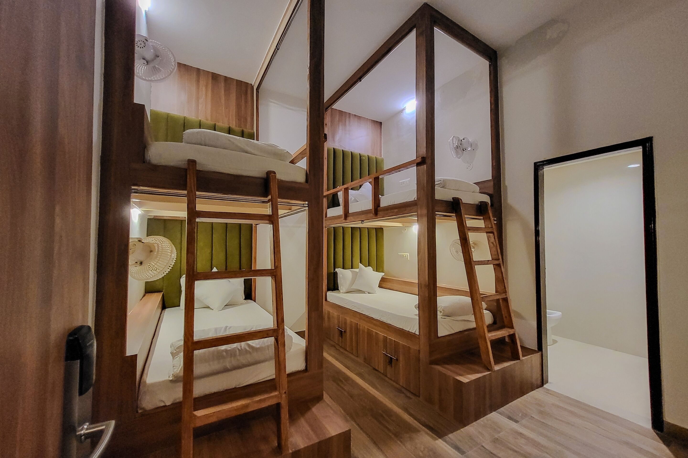 A room with bunk beds, wooden flooring, a green upholstered headboard, and a white ceiling fan.