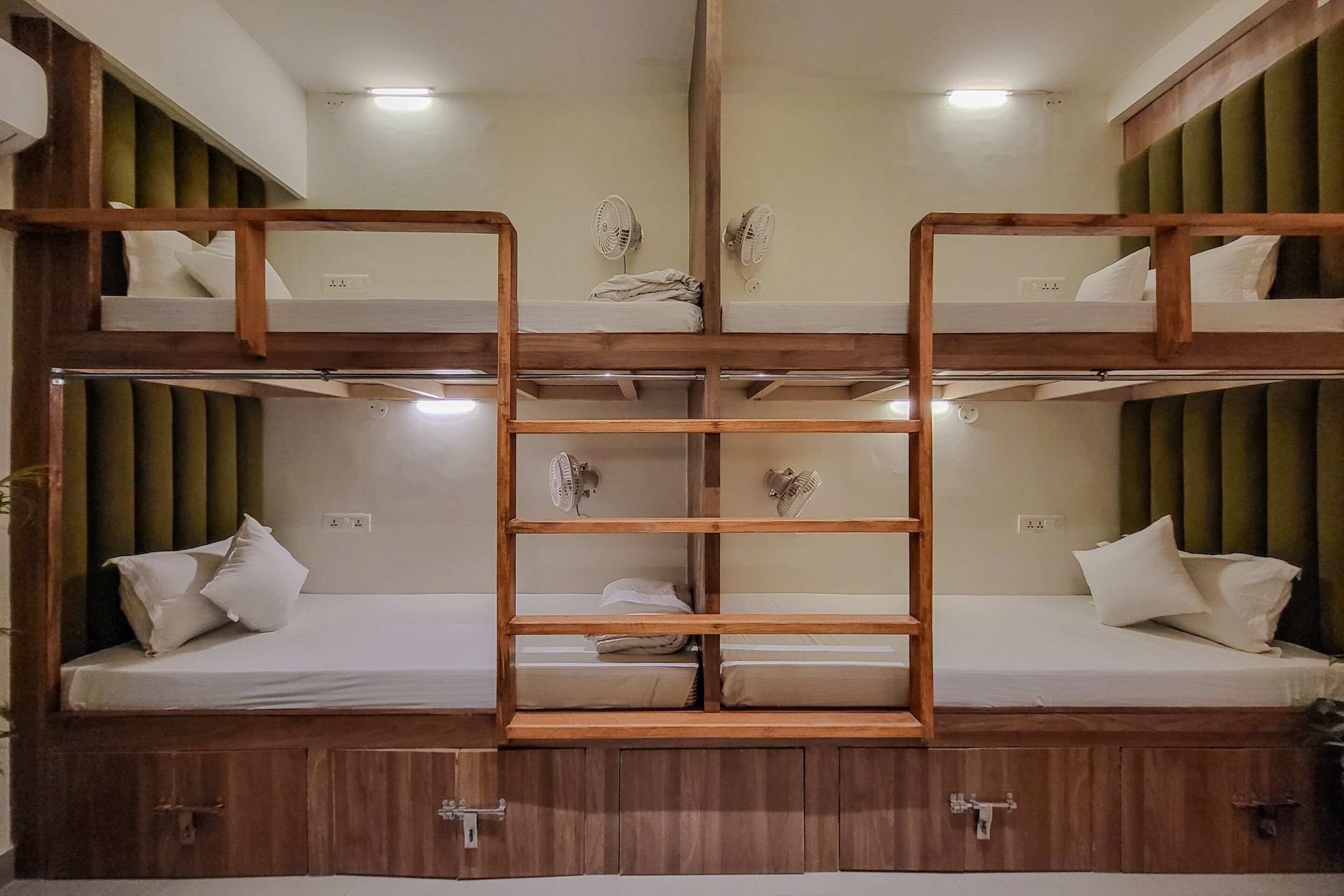A bunk bed room with a central ladder, wooden headboard, and bedside fans.
