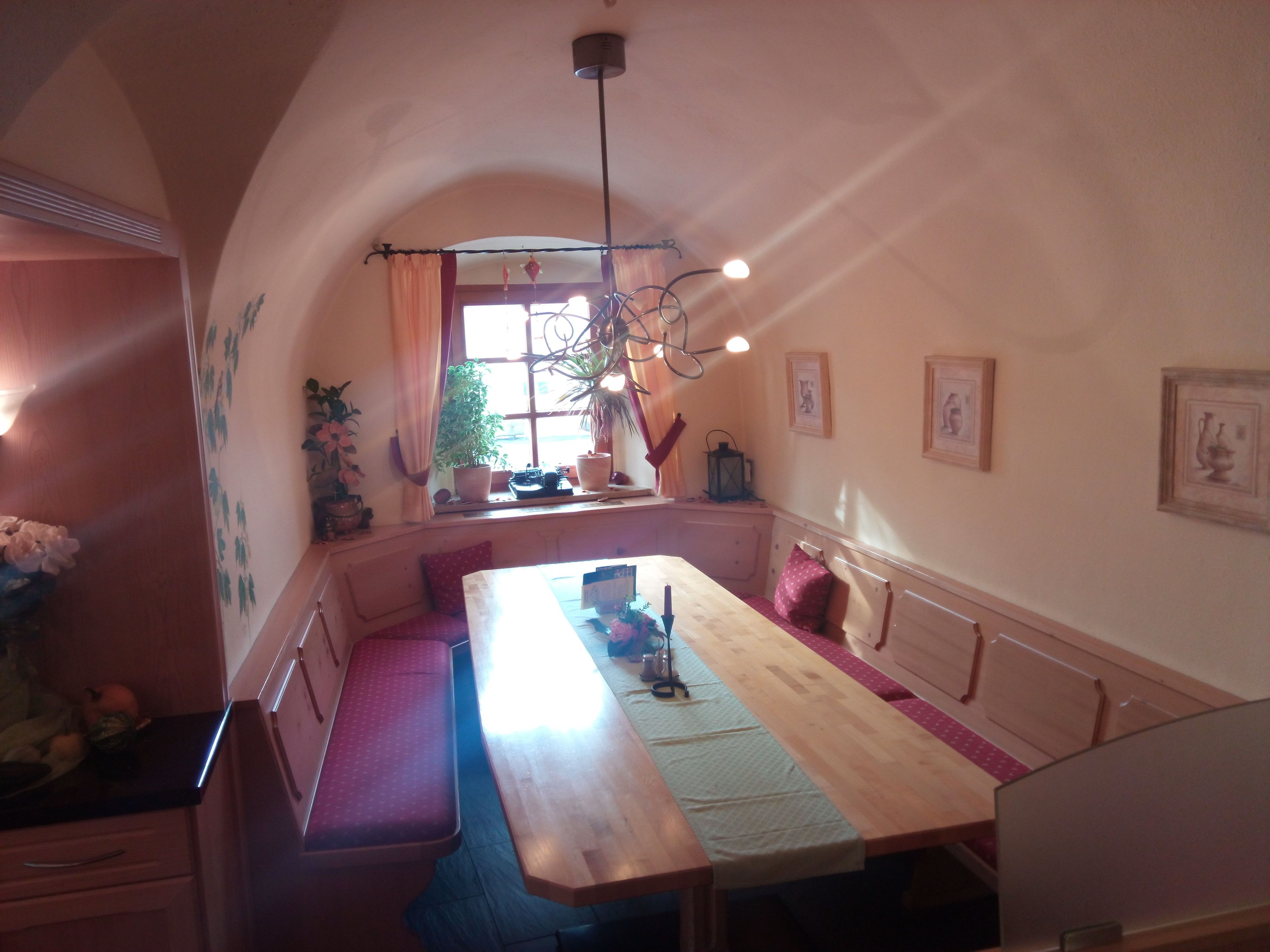 A cozy dining area with a wooden table and bench seating, a window with curtains, and a hanging light fixture.