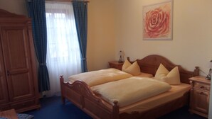 A double bed with wooden headboard and footboard, two bedside tables with lamps, a wooden wardrobe, and a painting of a rose on the wall. - Landgasthof Reichsadler (Hoechstaedt im Fichtelgebirge)