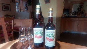 Two bottles of Echte Hochstadter Vogelbeertropfen wine on a wooden tray with three empty glasses. - Landgasthof Reichsadler (Hoechstaedt im Fichtelgebirge)