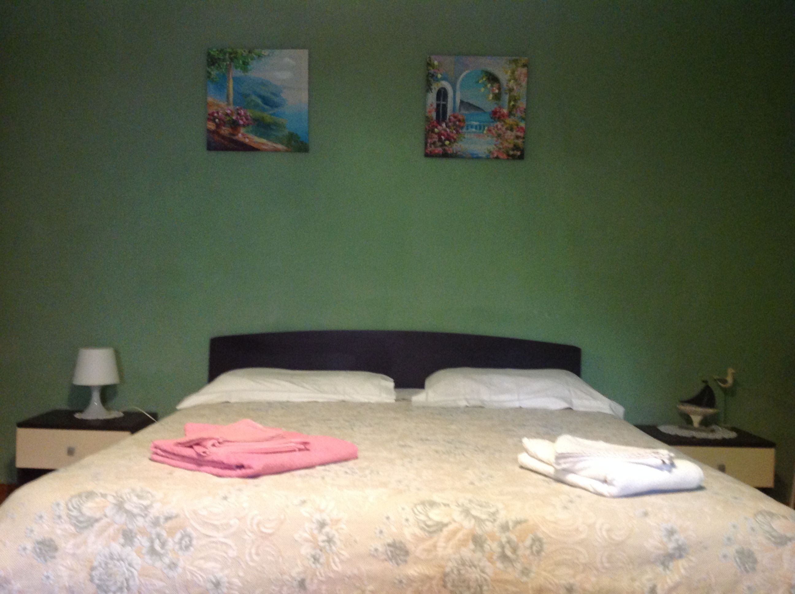 A neatly made bed with folded towels, a nightstand with a lamp, and two paintings on the wall.