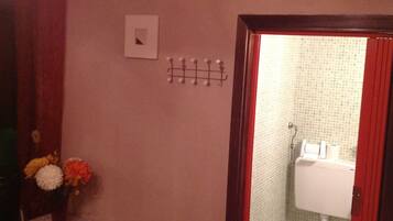 Un baño con inodoro, lavamanos y ducha. Hay un espejo, un perchero para toallas y una mesita con un jarrón de flores.