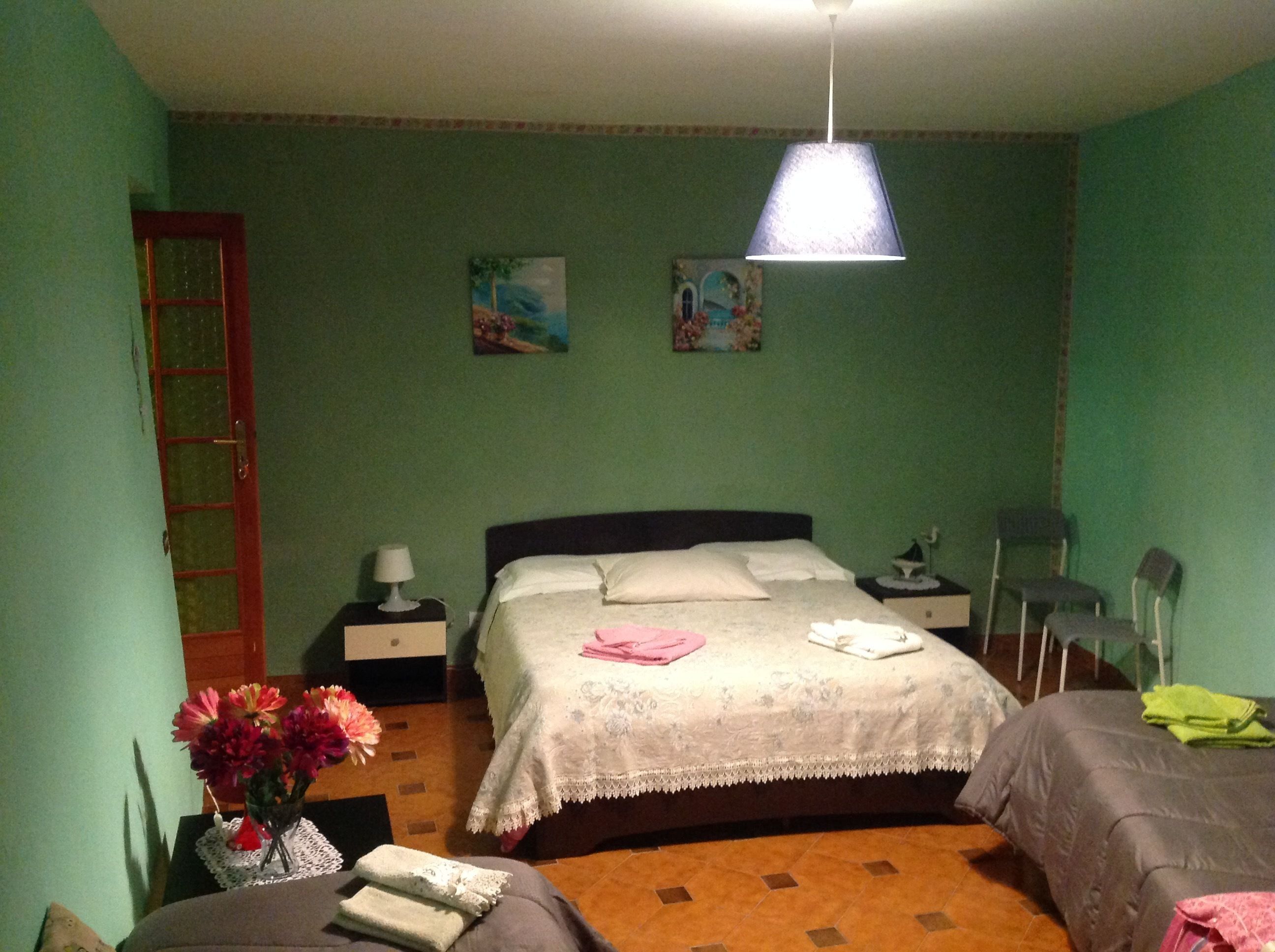 A bedroom with a bed, bedside tables, a nightstand, a lamp, a chair, a small table with a vase of flowers, and a painting on the wall.