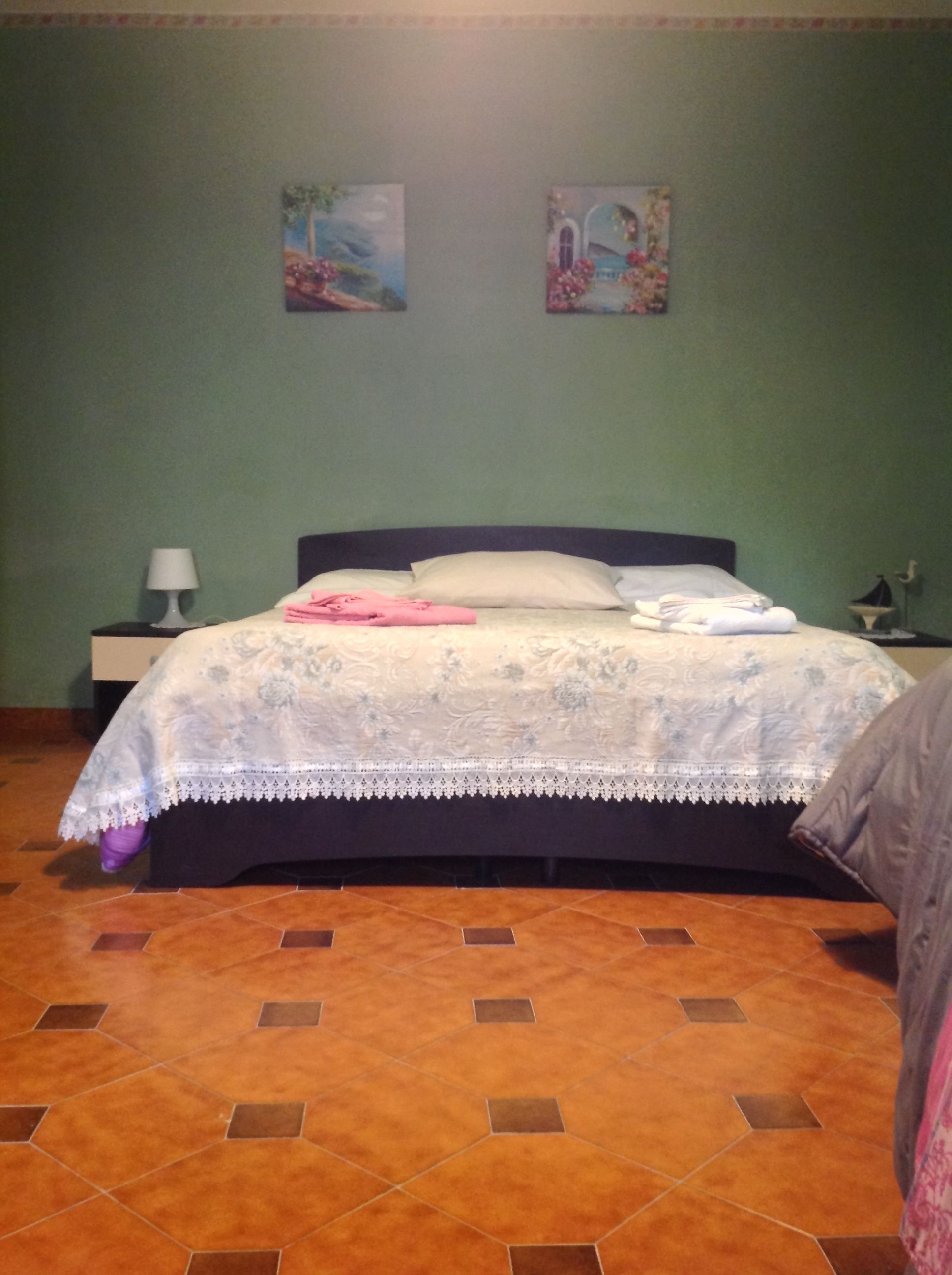 Ein Schlafzimmer mit einem Bett, einem Nachttisch, einer Lampe und zwei Wandbildern.